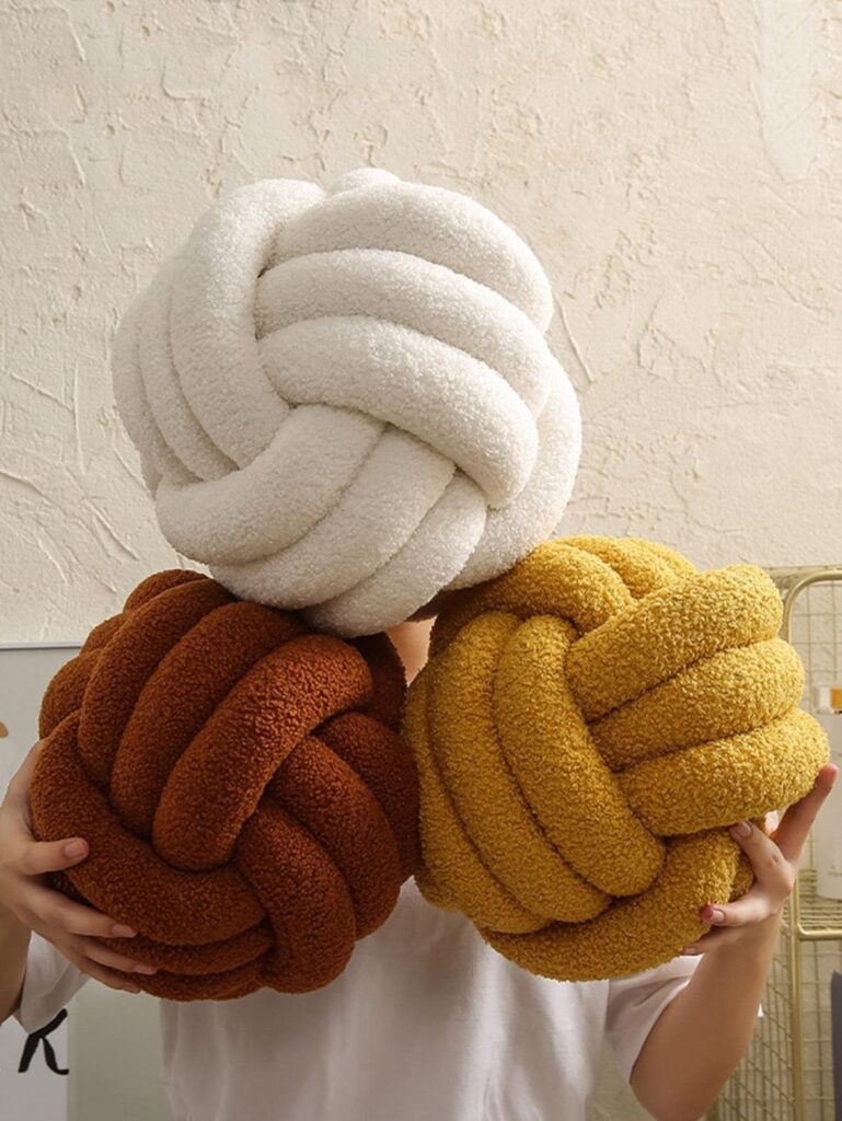 Cojín decorativo tipo nudo en textura suave tipo bouclé, diseño moderno que aporta estilo, confort y un toque exclusivo a cualquier espacio.